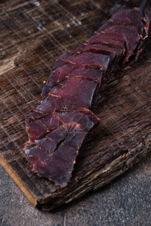 Photo for Homemade jerky meat on a kitchen cutting board, dark and moody, clouseup on a black wooden  background - Royalty Free Image