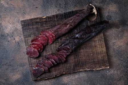 Photo for Two piece of homemade jerky meat on a kitchen cutting board, dark and moody, clouseup on a black wooden  background - Royalty Free Image