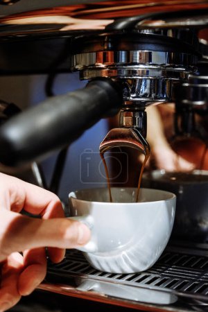 Foto de Espresso vertiendo de la máquina de café en la taza de café. Baristas mano sostiene una taza - Imagen libre de derechos