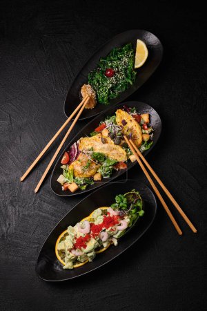 Téléchargez les photos : Chuka wakame, Cesare salad and Avocado salad and chopsticks in Japanese stile on a black concrete background. Top view - en image libre de droit