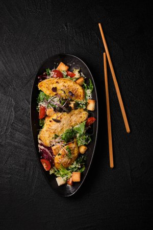 Téléchargez les photos : Caesar salad and chopsticks in Japanese stile on a black concrete background. Top view - en image libre de droit