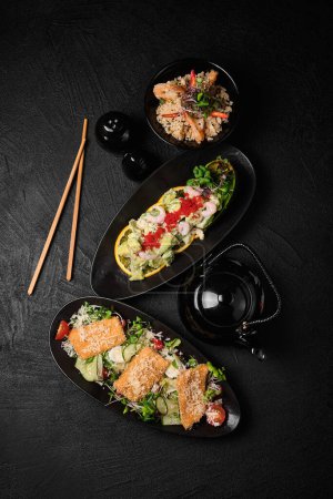 Téléchargez les photos : Caesar salad, avocado salad, rice and chopsticks in Japanese stile on a black concrete background. Top view - en image libre de droit