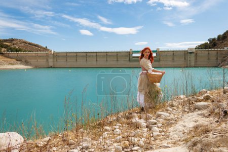 Portrait d'une femme habillée en paysanne vintage avec le barrage du réservoir d'Amador à faible niveau d'eau en raison du changement climatique, Espagne