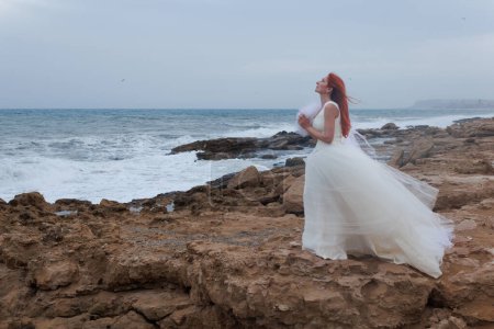 Mujer solitaria en vestido de novia rezando a los dioses un novio para la boda en el día ventoso en la costa del mar Mediterráneo, Alicante, España