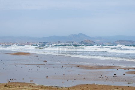 Starker windiger Tag über der Bucht von Alicante mit der Stadt im Hintergrund und starken Wellen vom Strand El Altet, Spanien