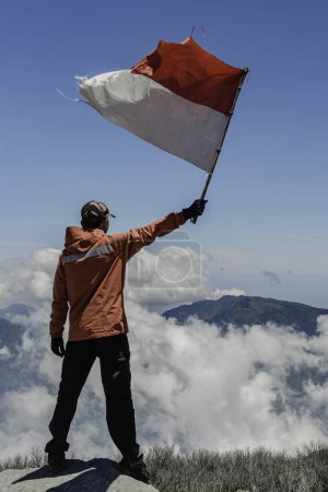 hombre asiático con bandera indonesia en la cima de la montaña bajo el cielo azul