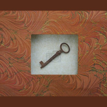 Photo for Antique rusty key with round hole placed in a frame on grey background frame of handmade marbled paper, in warm autumn colours, atmospheric minimalist scene, from the front - Royalty Free Image