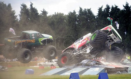 Foto de Paddock Wood, Kent, Inglaterra: 'Swamp Thing' y otro Monster Truck aplastan autos mientras corren alrededor de una gran carrera de obstáculos recibiendo aire para entretener a la multitud en un rally de Monster Truck. - Imagen libre de derechos