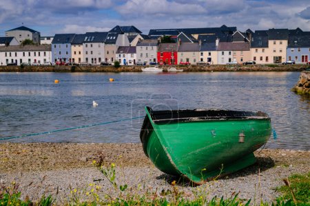 A green boat at shore with Galway's skyline in the background