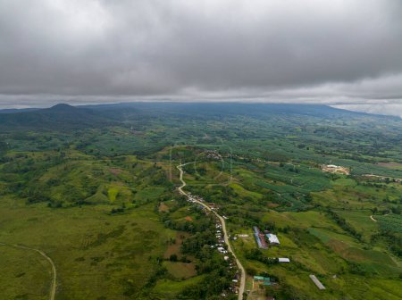 Foto de Drone vista de la montaña con tierras de cultivo en crecimiento y pequeño pueblo a lo largo de la carretera. Mindanao, Filipinas. - Imagen libre de derechos