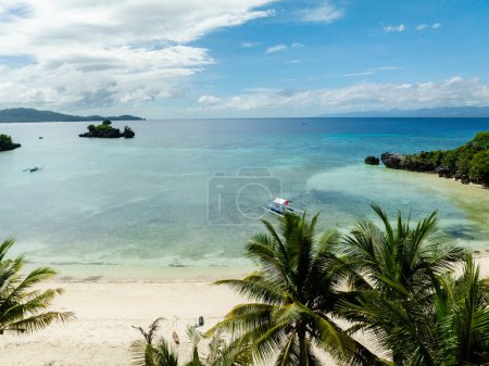 Boat floating over clear sea water in white beach, view from coconut trees in Cobrador Island. Romblon, Philippines.
