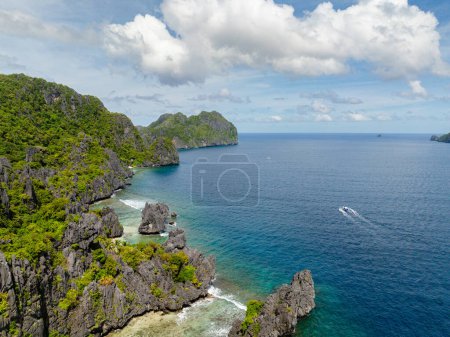 Coastline wiith rocas de piedra caliza y barco sobre el mar azul. Isla Matinloc. El Nido, Filipinas.
