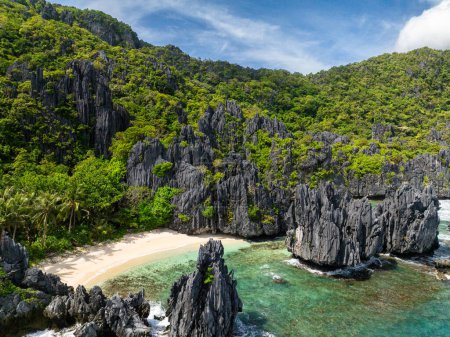 Des vagues océaniques et de l'eau claire s'écrasent sur des roches calcaires et une plage de sable. Île de Matinloc. El Nido, Philippines.