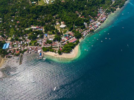 Coastline with houses and sandy white beach. Turquoise sea water with sunlight reflection. Samal Island. Davao, Philippines.