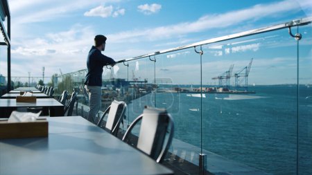 Millennial guy resting terrace at sea port view. Freelancer enjoying ocean view thinking life career problems. Successful businessman taking break relaxing on rooftop cafe. Peaceful morning concept.