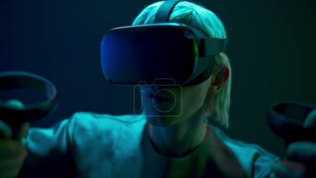 Foto de Excited man experiencing handheld trackpads videogame closeup. Impressed gamer using gadget for virtual reality on neon background. Futuristic goggles youngster playing. Future technology concept - Imagen libre de derechos