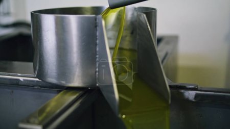 Téléchargez les photos : Unfiltered oil pouring container at factory closeup. Cold pressed olive liquid flowing in deep dish at facility. Centrifugal extraction of delicious organic extra virgin product at manufactory - en image libre de droit