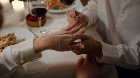 Photo for Man hands wearing engagement ring at romantic dinner close up. Unknown guy proposing marriage to woman at evening. Two lovers sitting candles atmosphere at night interior. Celebrating wedding proposal - Royalty Free Image