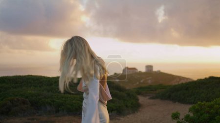 Blonde tourist posing at castle valley. Cute woman watching sightseeings enjoying sea vacation. Girl stepping spinning field at sunset evening. Traveling lady dress relaxing autumn nature landscape