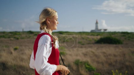 Inspired lady travelling at lighthouse closeup. Calm tourist woman carrying digital camera on neck outdoor. Happy photographer shooting autumn landscapes during weekend. Vacation adventures concept
