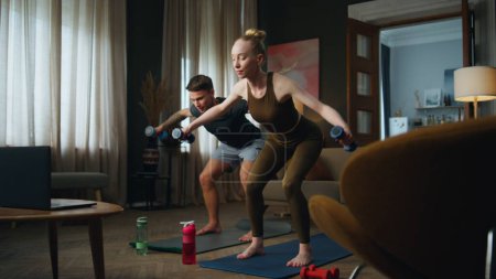 Photo for Active millennial family training with dumbbells at home. Smiling young couple making sport exercises for strong arms watching online lesson on laptop. Happy woman workouting with athletic man. - Royalty Free Image