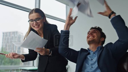 Téléchargez les photos : Des managers souriants jetant des papiers au bureau. Deux gestionnaires célèbrent la réussite du projet de finition contractuelle. Chers collègues, les gens d'affaires qui font un geste cinq apprécient le triomphe. Concept de victoire d'équipe - en image libre de droit