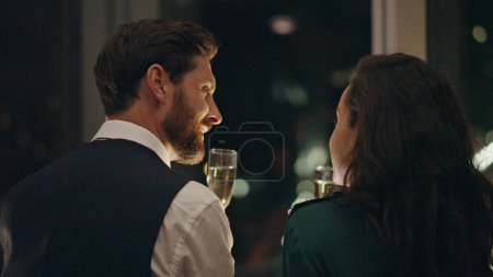 Photo for Smiling happy couple enjoy romantic evening with champagne standing at window close up. Young lovers relaxing drinking alcohol together. Bearded man flirting with brunette woman enjoying lovely date. - Royalty Free Image