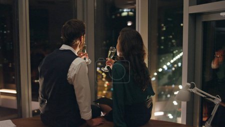 Photo for Attractive man seducer flirting woman drinking champagne celebrating successful project together. Couple coworkers in love talking sitting at panoramic window enjoying night city view. Romance concept - Royalty Free Image