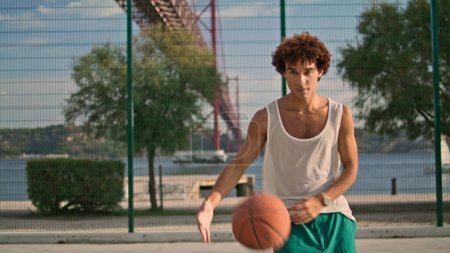 Photo for Contemporary student throwing ball at stadium closeup. Young man playing at open air playground alone. Muscly basketball player demonstrating skills looking camera. Sport healthy lifestyle concept - Royalty Free Image