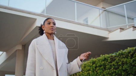 Mujer segura caminando por los suburbios de la calle. Magnífico afroamericano agente de bienes raíces tienen llaves pasear por el barrio. Elegante mujer de negocios conmutar a casa por la noche. Inmobiliaria propietario ir a la reunión del cliente