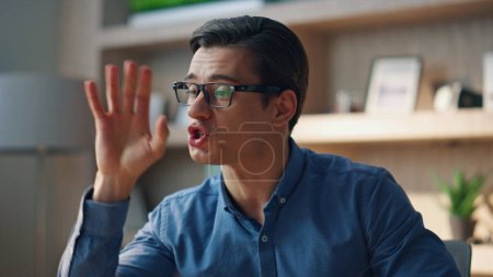 Photo for Closeup angry businessman yelling videocall at modern cabinet. Nervous manager gesturing hand speaking computer video chat at office. Eyeglasses stressed man talking on raised tones arguing at room - Royalty Free Image