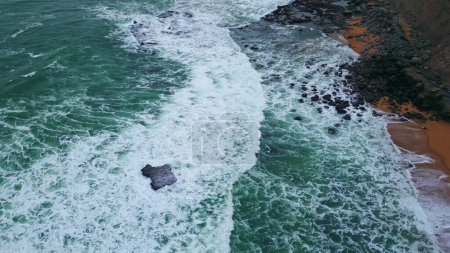 Téléchargez les photos : Eau moussante agitant des rochers de plage près. Superbes vagues de mer agitées couvrant le littoral se déplaçant au ralenti super faible. Paysage marin océanique pittoresque marée piscines. Incroyable mousse surf lavage galets - en image libre de droit
