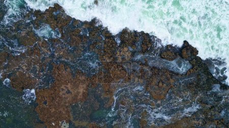 Téléchargez les photos : Eau tourbillonnante moussant falaises côtières zoom arrière. Vue de drone supérieur vagues de mer rugueuses rupture de pierres sombres volcaniques. Ruisseau orageux de l'océan s'écrasant de dangereux littoral rocheux. Paysage marin à couper le souffle - en image libre de droit