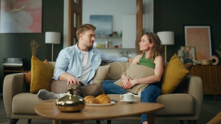 Photo for Resting couple talking at cozy sofa interior. Cheerful man gesturing hands telling story. Love couple sharing dreams having breakfast at modern home. Young family daydreaming together feel carefree - Royalty Free Image