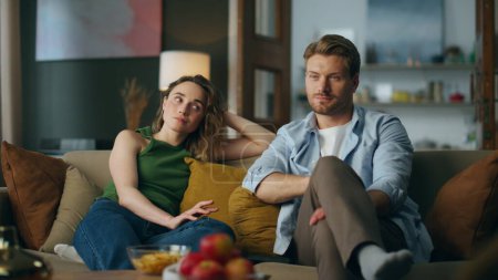 Photo for Bored spouses watching movie feeling disinterested at home. Smiling man woman looking each other started laughing at sofa. Love pair staring stupid tv show sitting at living room. Online entertainment - Royalty Free Image