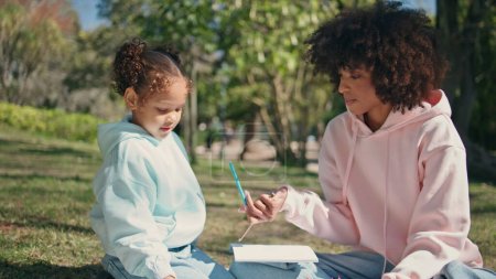 Photo for Woman daughter enjoy creativities sitting green meadow at weekend picnic close up. Curly african american mother giving colorful pencil to little child outdoors. Carefree happy family painting in park - Royalty Free Image