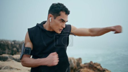 Photo for Strong boxer workout seaside closeup. Professional athlete punch air on cliff. Serious motivated sportsman training kickboxing in morning. Muscular guy practice looking camera. Outdoor cardio exercise - Royalty Free Image