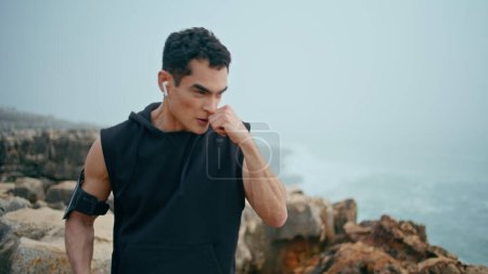 Photo for Closeup boxer guy training on cliff mountain. Focused strong athlete boxing air kickboxing in cloudy seaside. Motivated professional sportsman workout prepare for fight. Strength endurance concept. - Royalty Free Image
