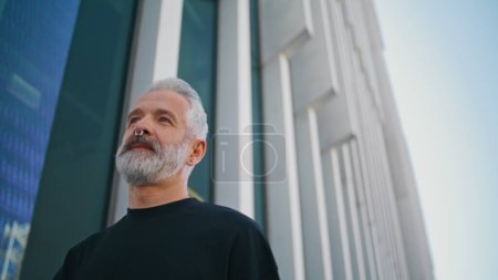 Photo for Mature man walking urban street closeup. Thoughtful bearded senior go downtown in morning. Successful elderly businessman resting strolling outdoors. Good looking grey hair senior wear nose piercing - Royalty Free Image