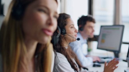 Telemarketing team working office together. Smiling woman specialist consulting customer on call. Helpful joyful agent talk give instructions. Hotline operators colleagues helping clients in office.
