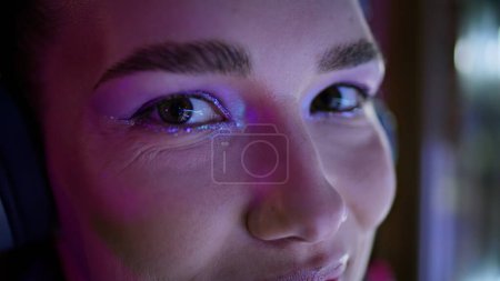 Closeup beautiful smiling woman eyes with modern bright makeup lit by soft lamp. Portrait of attractive happy girl wearing wireless headphones. Gorgeous young lady listening music feeling happiness.