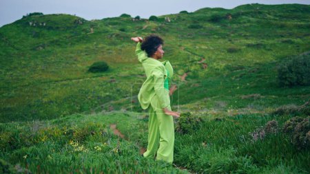 Confident modern style dancer moving body professionally on evening green field. African american woman contemporary dancer performing expressive dance at cloudy nature. Curly girl artist dancing.