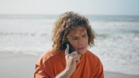 Worried handsome guy talking smartphone at summer sea vacation close up. Attractive thoughtful man speaking on modern telephone looking beautiful seascape. Curly boy relaxing on ocean coast with phone