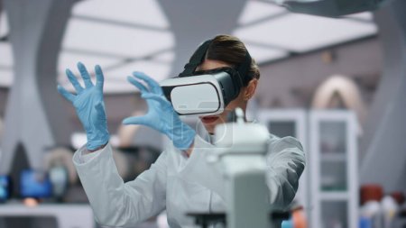 Virtual headset bioengineer researching augmented reality in futuristic medical laboratory close up. Woman lab worker using vr goggles in science clinic. Scientist working in hi-tech neuroscience.