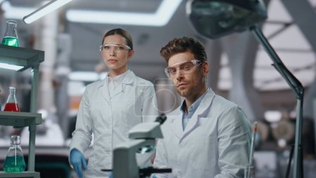 Téléchargez les photos : Portrait rapproché de deux chercheurs médicaux portant des gants de lunettes de protection à l'équipement clinique d'innovation. Scientifiques professionnels confiants posant en laboratoire avancé. Les jeunes médecins regardent caméra. - en image libre de droit