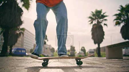 Jambes patineur extrême sautant sur longboard à la rue ensoleillée de près. Jeune skateboarder méconnaissable effectuant flip trick au ralenti. Inconnu homme énergique de formation passe-temps à la soirée d'été.