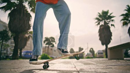 Primer plano skateboarder piernas entrenamiento kickflip en monopatín día soleado. Hombre de moda desconocido patinador aprendizaje truco extremo con longboard en cámara lenta. Hipster activo saltando practicando patinaje en la calle