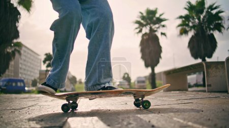 Pieds skateboarder effectuer tour avec longboard à la lumière du soleil d'été à l'extérieur. Homme inconnu hipster pratiquant kickflip sur la rue ensoleillée de près. Homme actif jouissant d'un passe-temps extrême au ralenti.