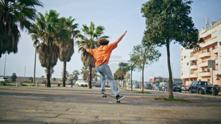 Patineur extrêmement cool pratiquant le skateboard dans la rue de la ville. Adolescent sportif effectuant des tours de skate près des paumes. Jeune hipster jouissant d'un passe-temps actif l'été. Sportsman entraînement patinage au ralenti