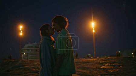 Photo for Loving teenagers looking eyes to eyes at night beach. Romantic pair dating at evening zoom on. Smiling man whispering tender words to lovely girlfriend. Affectionate couple enjoying moment together - Royalty Free Image